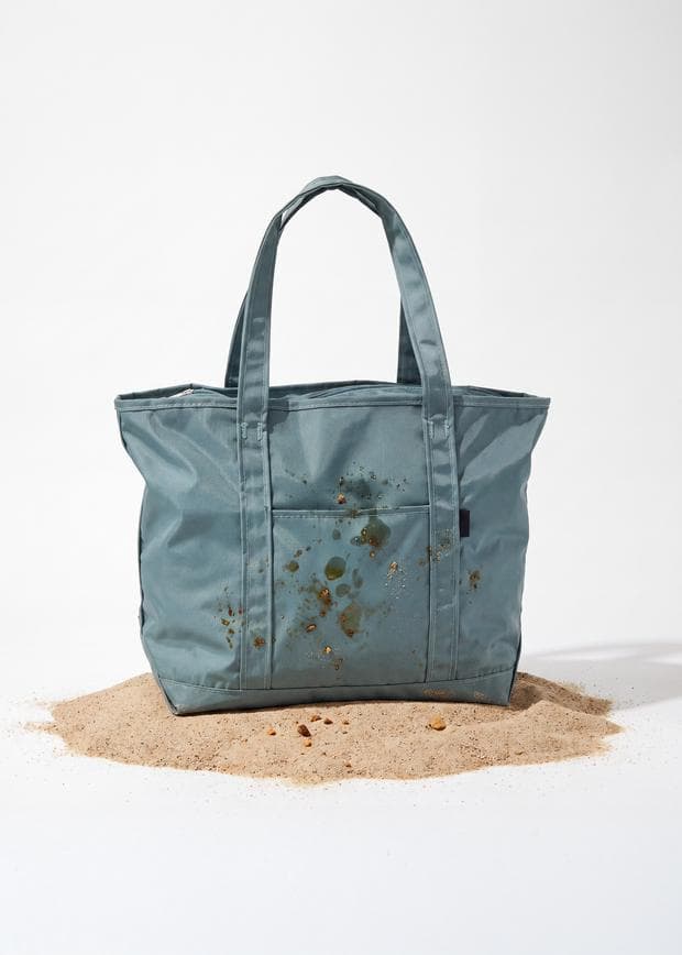 An ordinary canvas beach tote, stained and sitting on a pile of sand